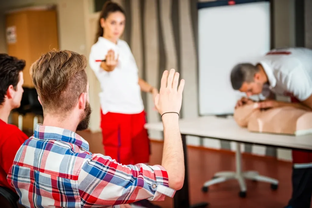 Student raising a hand during a first aid class while an instructor teaches